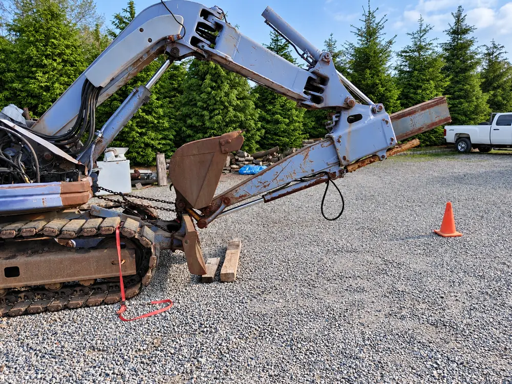 Mini excavator with its boom and arm collapsed to the ground, chained and blocked up in the yard while it waits on excavator parts